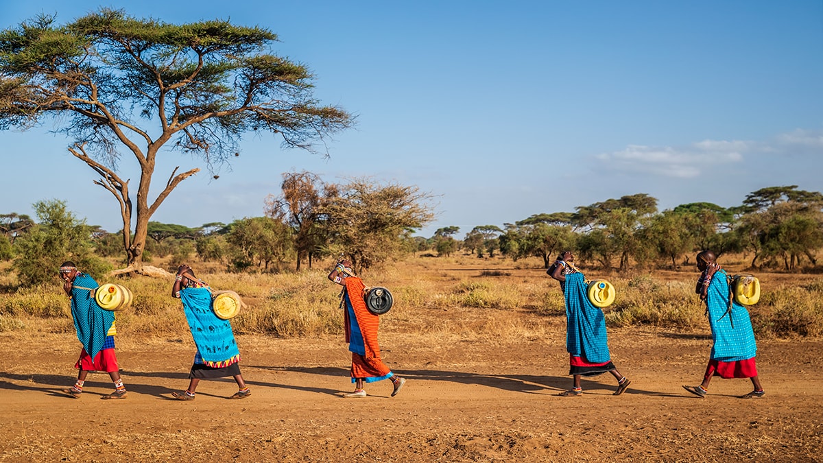 GettyImages_GlobalHealth_1200x675 Global Health Observances - people wearing colorful patterned clothing walk barefoot across a dirt road.