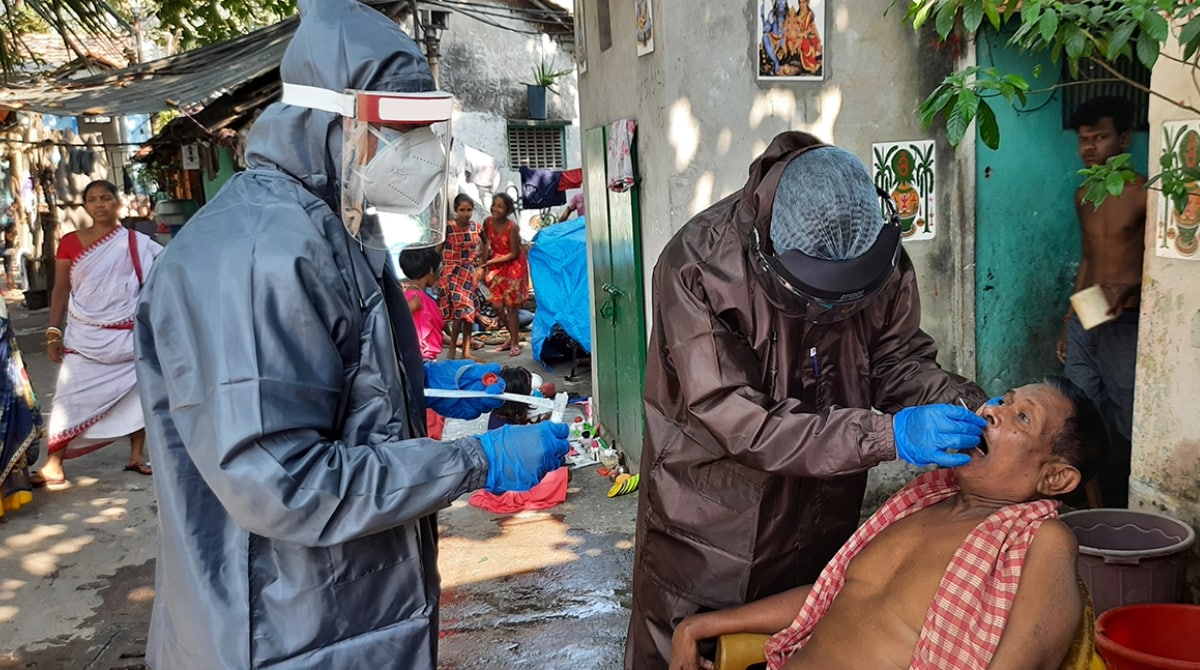 India_COVID19_16x9 Two nurses in protective gear swab a man's mouth in an outdoor setting.