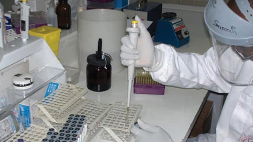 cote-d-ivoire-banner-large-16x9 Photo of laboratorian wearing personal protective equipment and holding a pipette over a test tube sitting in a test tube rack.