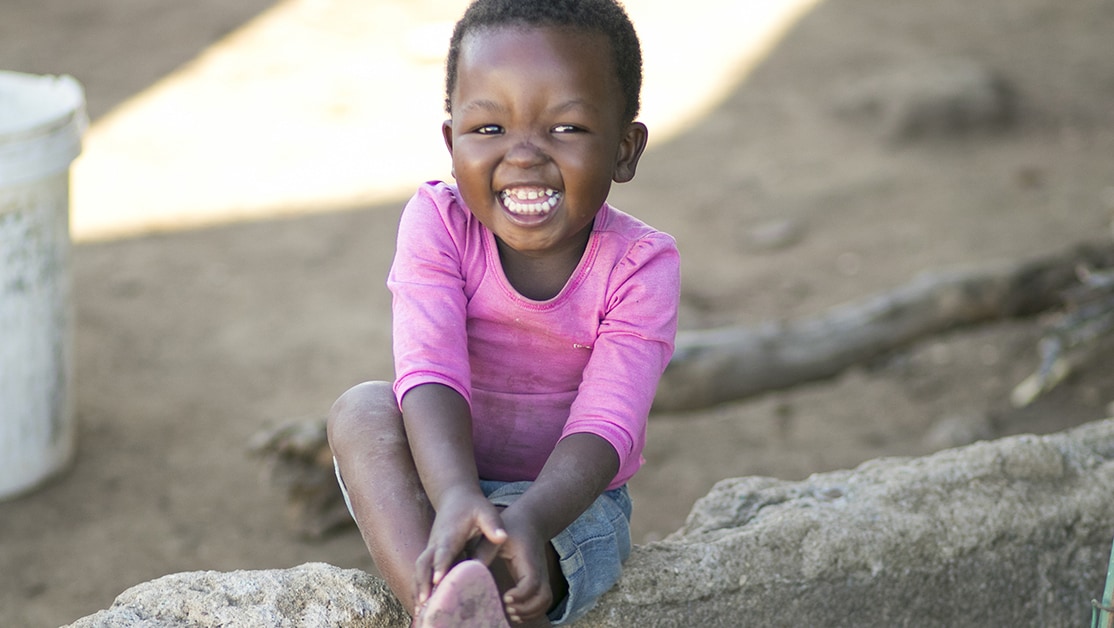 A young girl in a pink shirt smiles while sitting.