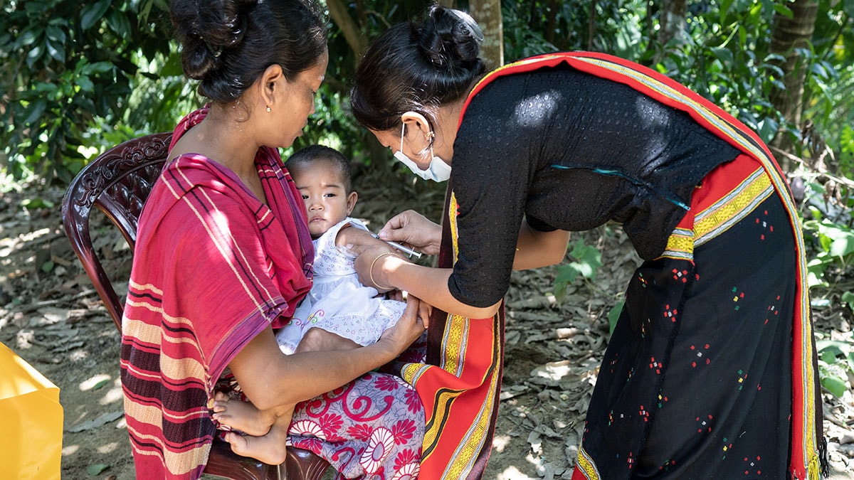 A woman holds a baby while a healthcare worker injects a vaccine