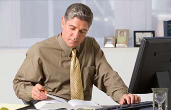 man-book-computer.jpg Man looking at a book while typing on a keyboard.