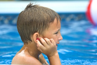 swimming boy touching his ear Niño en la piscina poniéndose tapones para los oídos.