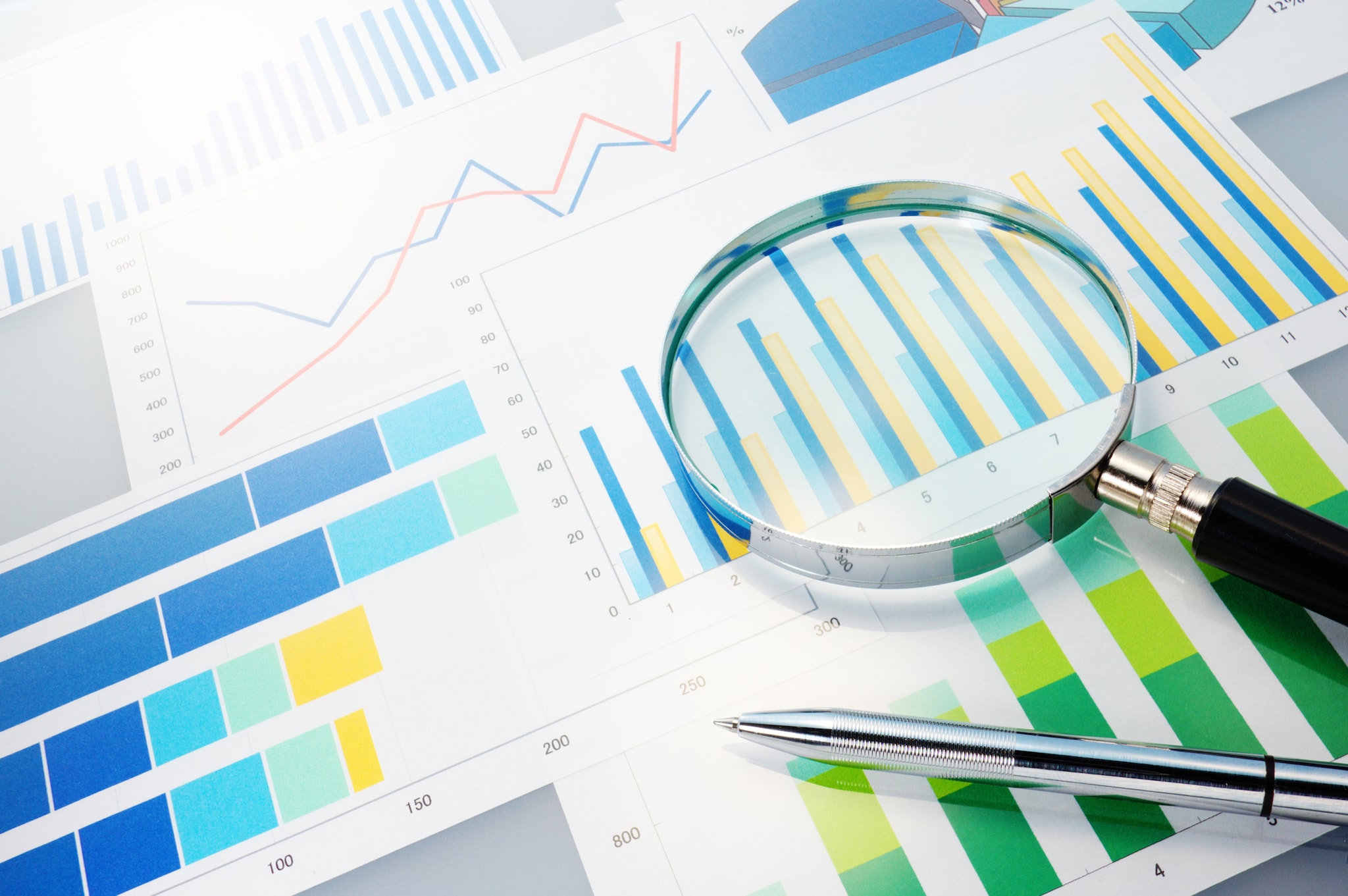 — title missing — Silver pen and magnifying glass on top of blue and green charts and figures