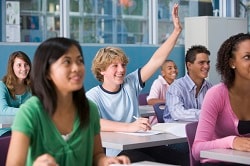 Teenagers in class, one with hand raised Teenagers in class, one with hand raised