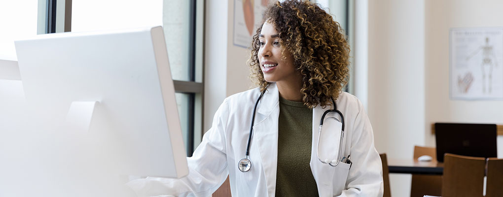 Adult female doctor reviews patient records on desktop PC. Adult female doctor reviews patient records on desktop PC.