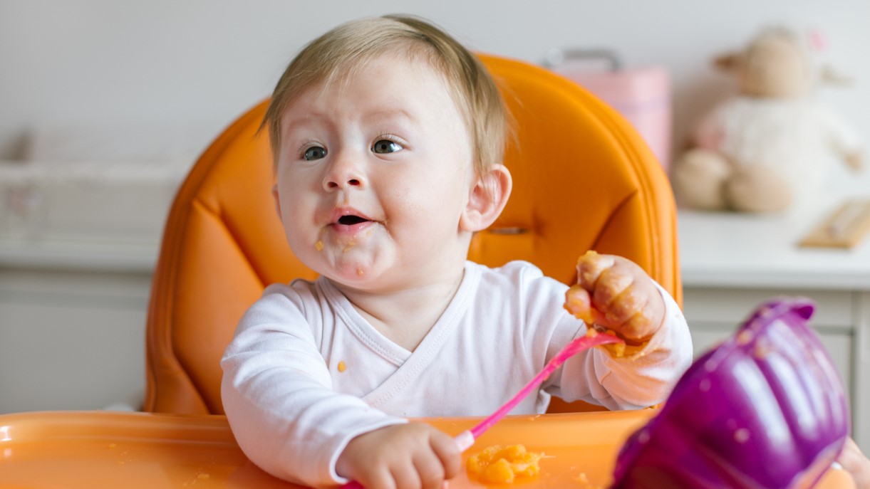 baby girl in high chair Young baby eating pureed food with hands sitting in highchair.