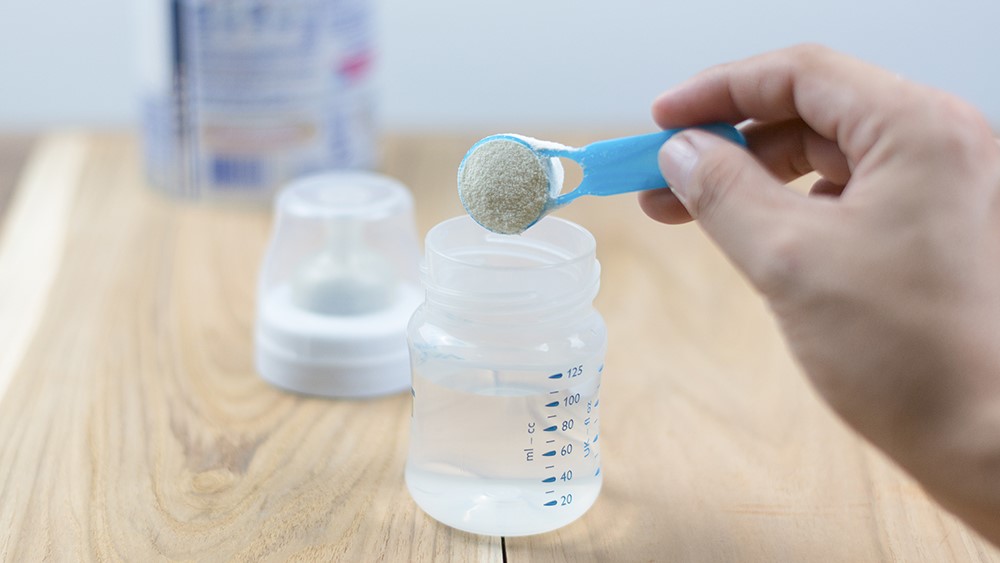 Formula preparation A person preparing infant formula in a bottle.