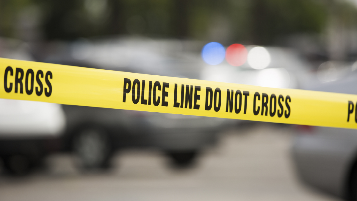 This figure shows a yellow tape that reads “Police line do not cross” with a blurred police car in the background.