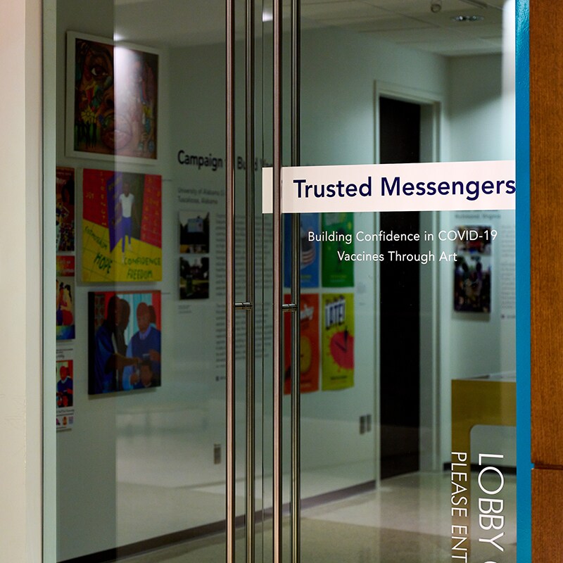 Photograph of gallery door with exhibition name "Trusted Messengers: Building Confidence in COVID-19 Vaccines Through Art" printed onto glass.