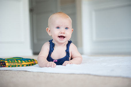newmilestoneMatter-header-2021 Young baby laying on tummy and smiling