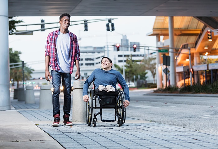 6-two-men-talking-one-wheelchair Two men talking while walking down the street. One man is in a wheelchair.