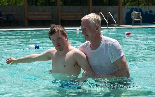 boy-man-pool-500px.jpg Boy with Down Syndrome in a pool with a man helping him.