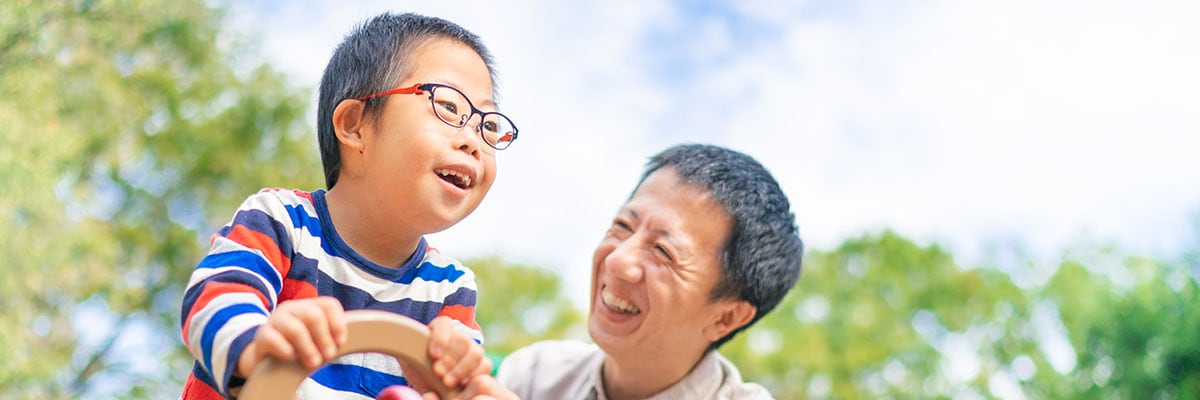 A small child with down syndrome is enjoying with his father at a public park on a sunny day.
