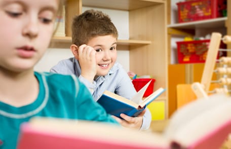 Boy looking up from book at a girl reading a book. Boy looking up from book at a girl reading a book.