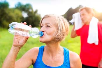 Senior woman drinking from a water bottle outdoors with senior man wiping his face with towel. Senior woman drinking from a water bottle outdoors with senior man wiping his face with towel.