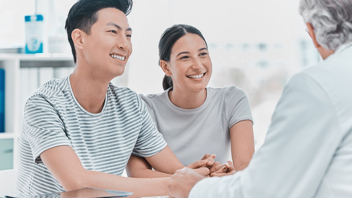 Smiling couple shakes hands with doctor