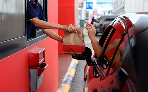 Hand of a person going through a fast-food drive-thru and accepting a food bag from a service worker through their car window