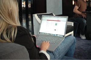 A young-looking woman with long blond hair sits on a chair in what looks to be an internet café.