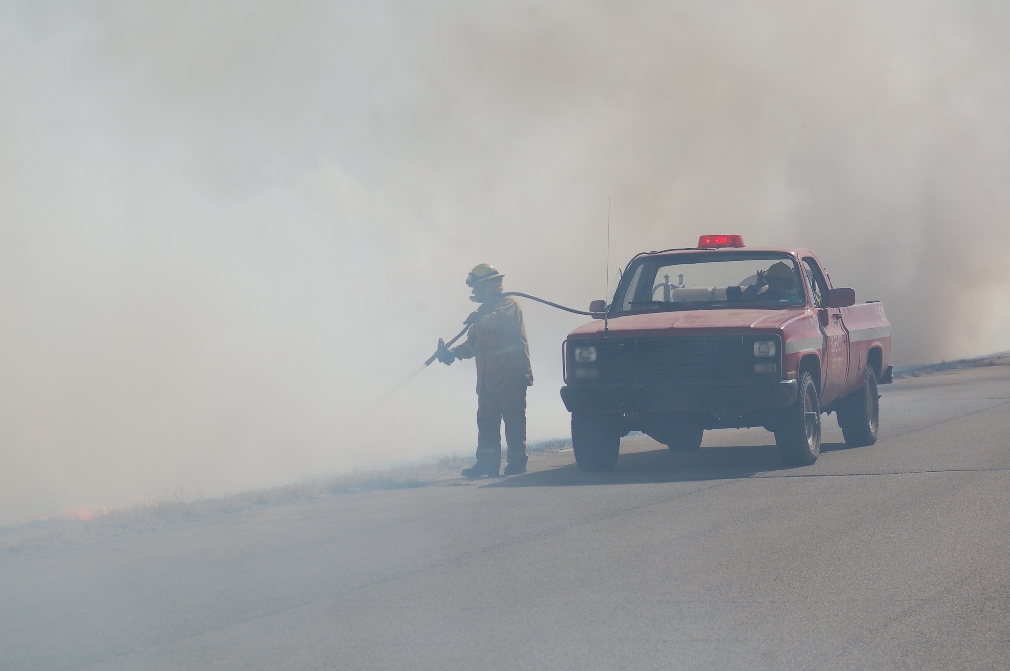 The FF using a booster hose to extinguish a very smoky grass fire