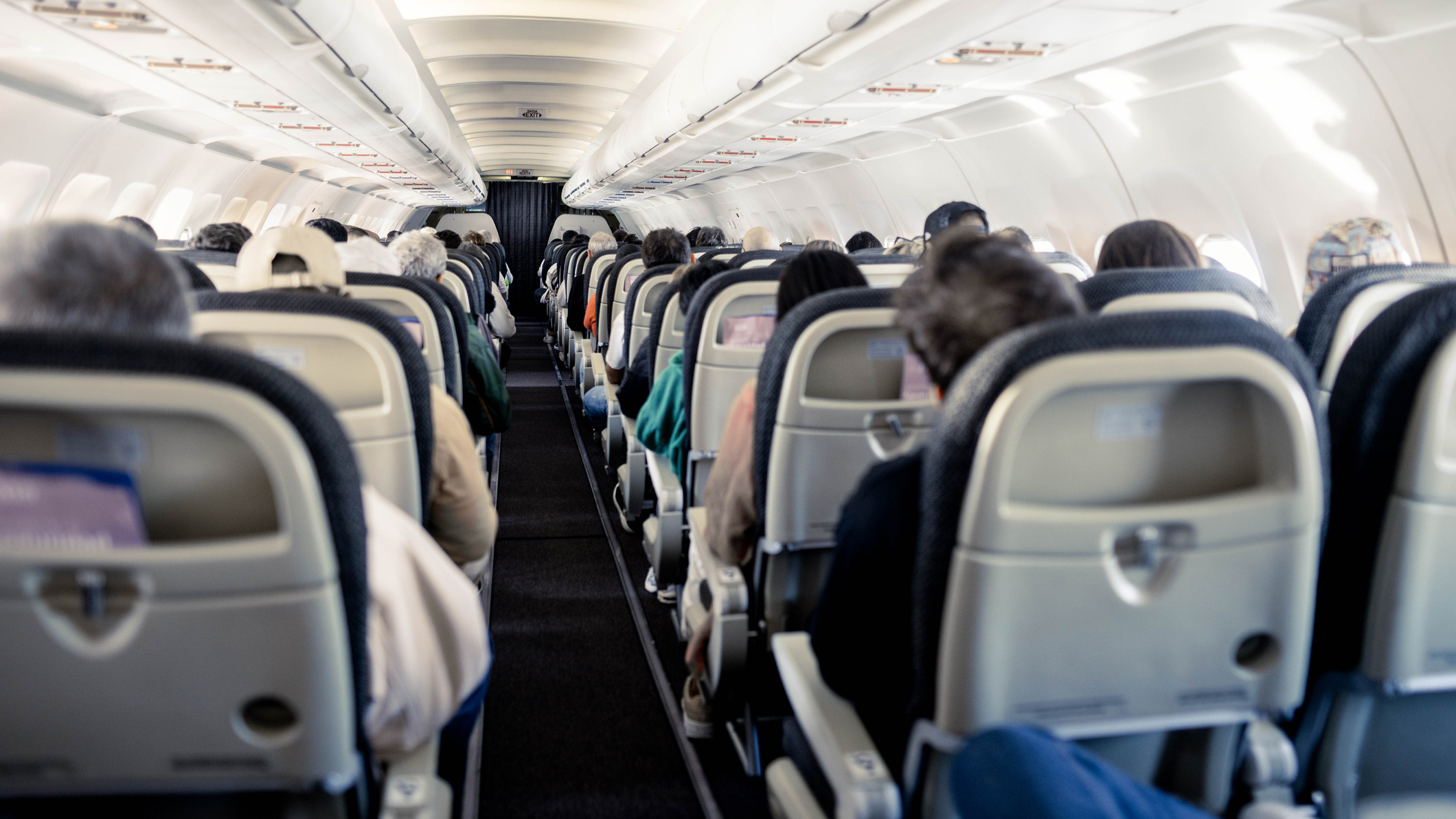 1674500771 Cabin of a commercial aircraft and seated passengers shown from the rear of the cabin.