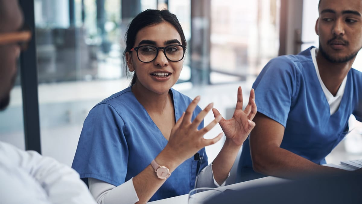 Advocating for Impact Wellbeing Guide 2 Nurse gestures with hands while talking to colleagues at a conference table.