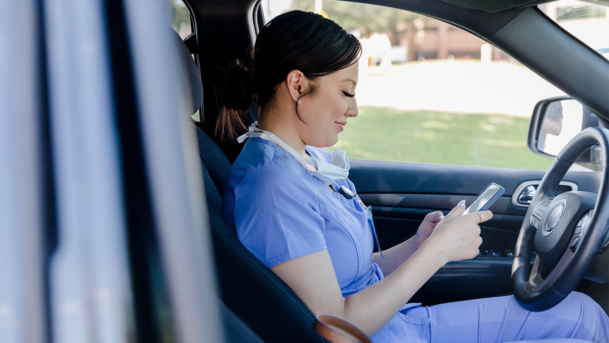 Advocating for Guide Use 3 Healthcare worker in scrubs looks at her phone while sitting in the driver's seat of a parked car.