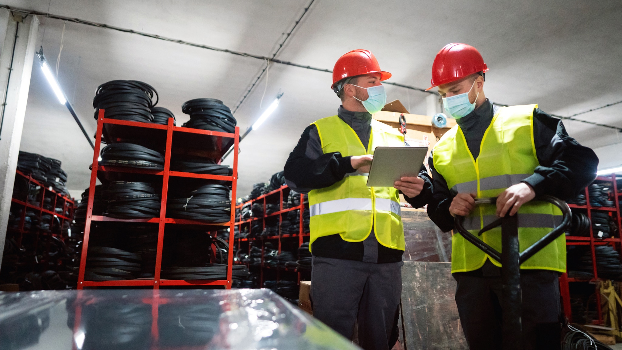 1298924655 Two workers wearing PPE look over papers on a clipboard in an industrial setting.