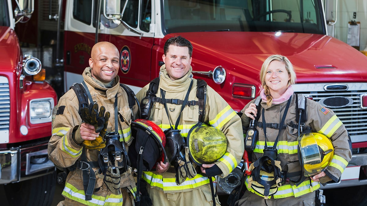 473421900 Group of structural firefighters standing in front of trucks with gear