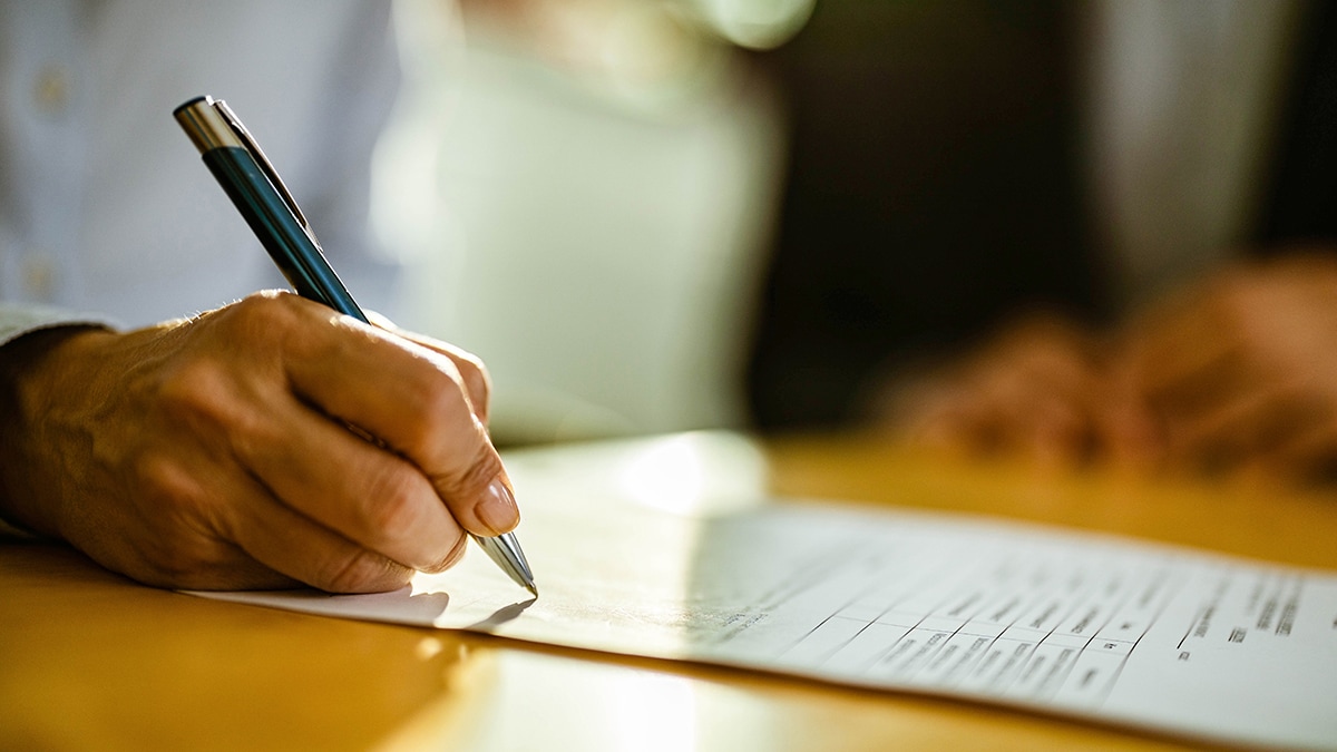 — title missing — a hand holding a pen writing on a white piece of paper on top of a wooden tabletop