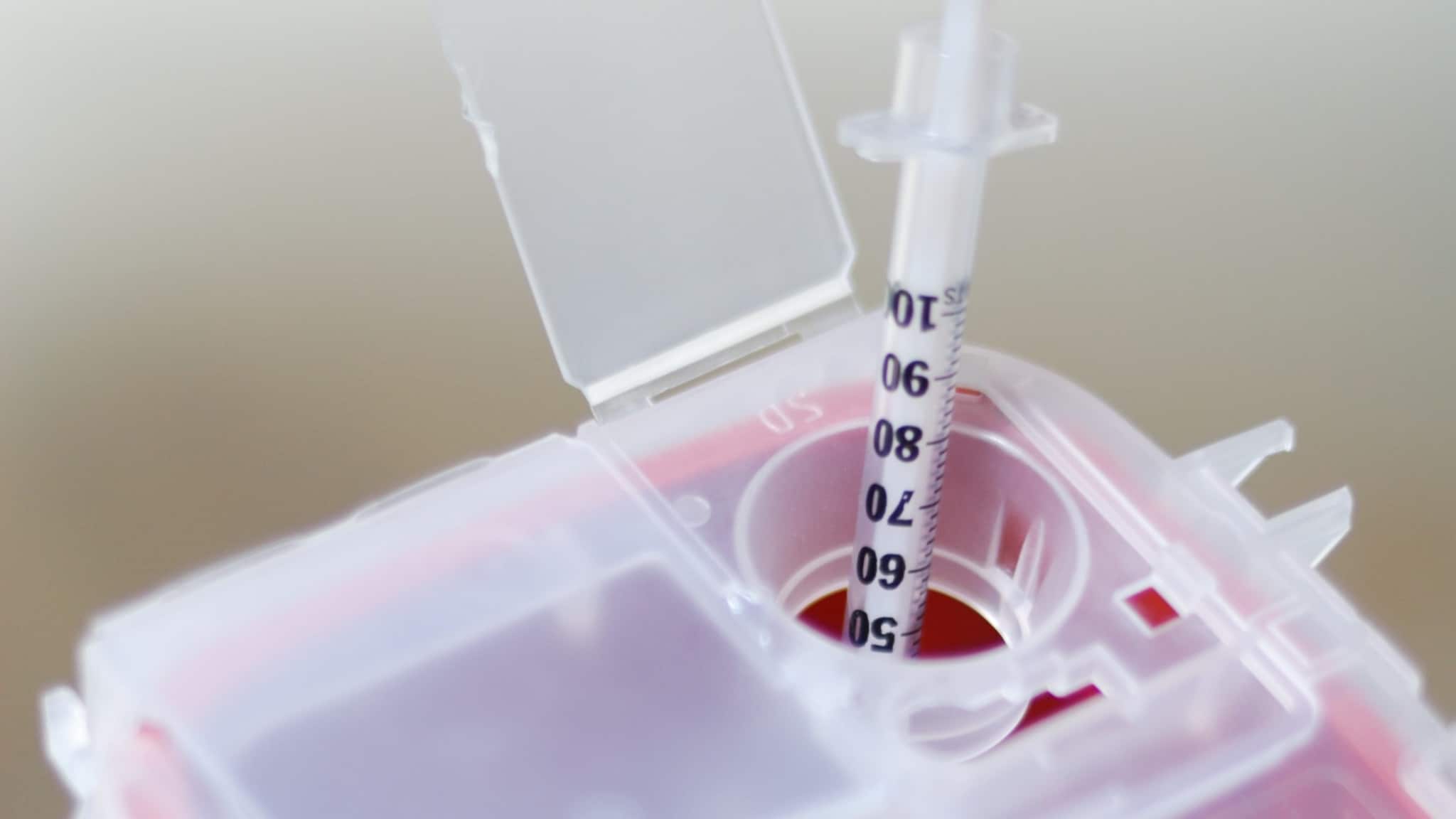 -- title missing -- A needle being placed in a sharps disposal container.