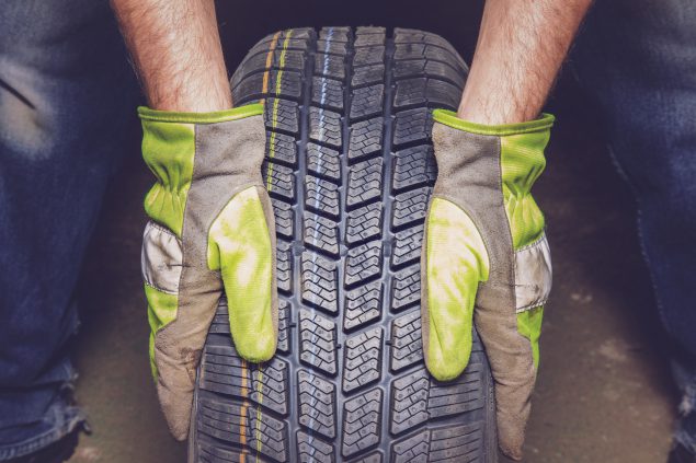 Man holding new, black rubber tire in the garage. tire