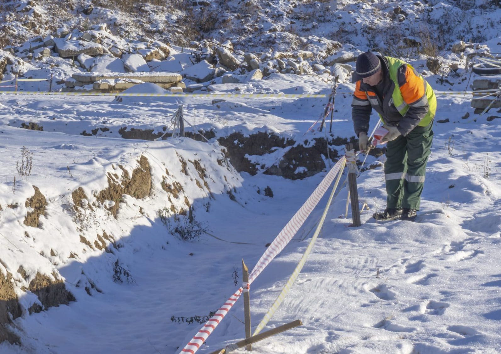 A worker at a construction site shields trenches with a signal tape for cadastral surveying.