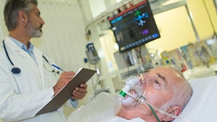 patient wearing oxygen mask on hospital bed with dr charting at bedside patient wearing oxygen mask on hospital bed with dr charting at bedside