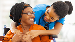 older woman with headwrap embraced from behind by younger medical professional