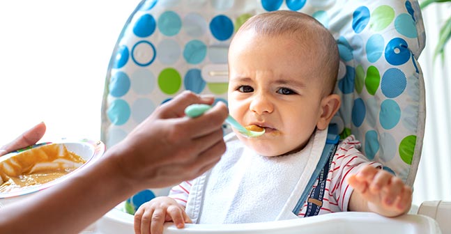 Baby in highchair reacts negatively to baby food.
