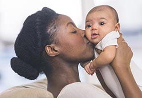 signs-hungry-full-2.jpg A mother raising her infant towards her and kissing her. The infant has soft, tranquil face.