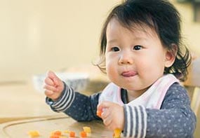 signs-hungry-full-3.jpg An older infant placing food into her mouth with her hands.