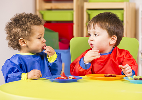 Two young boys eating at a green table in a childcare setting