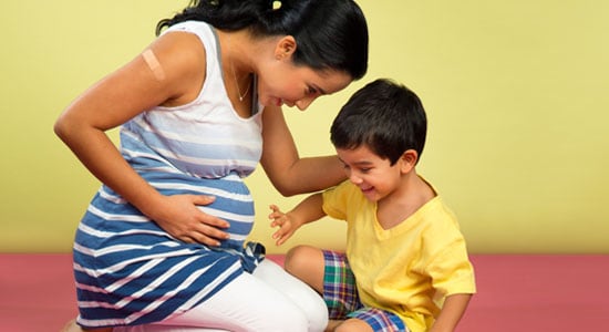 Pregnant mom and her toddler touching her belly and smiling.