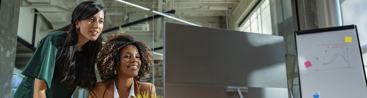 Two mixed race businesswoman looking at computer monitor in office.
