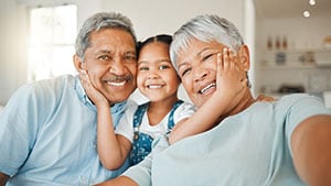 Grandparents snuggle with their granddaughter on a couch.