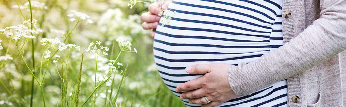 Pregnant women in a field holding her belly. 