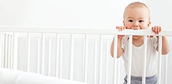 Infant standing up in crib teething on crib rail