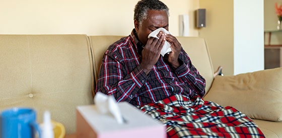 Man sitting down and blows his nose into a tissue