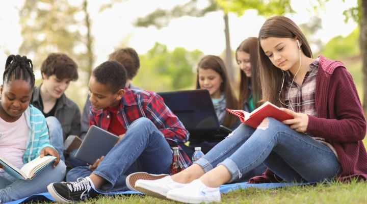 Grupo de jóvenes sentados afuera leyendo.