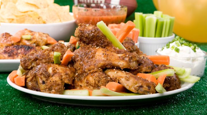 Plato de alitas de pollo frente a una pelota de fútbol.