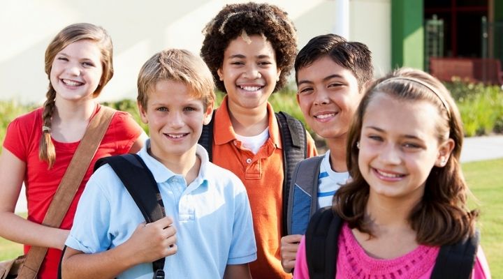 Un grupo de niños y niños con mochilas sonriendo.