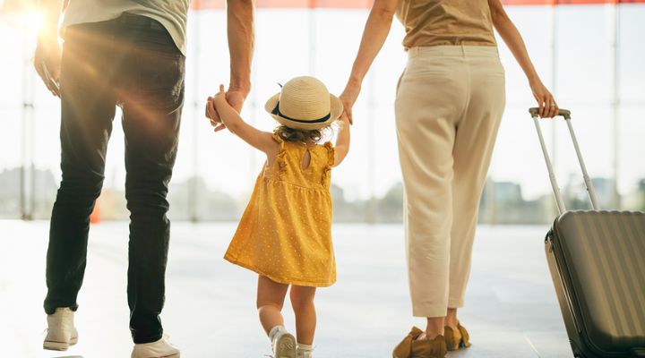 Padres sosteniendo la mano de su hija y caminando por un aeropuerto.
