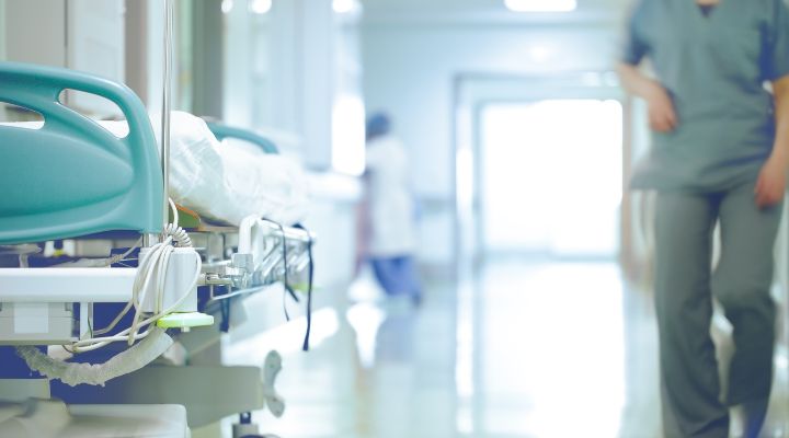 Pasillo del hospital con una cama y un trabajador médico caminando.